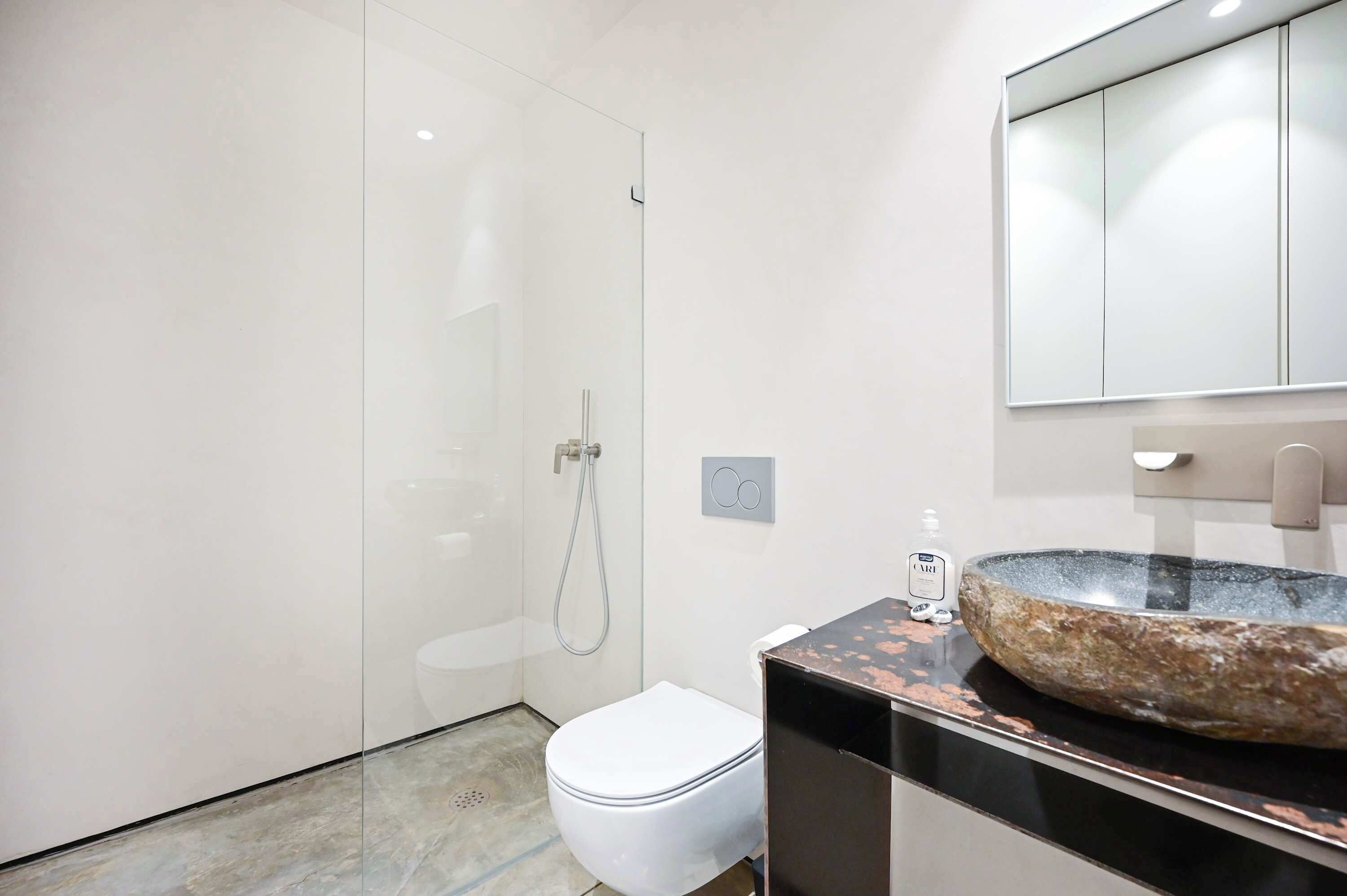 Ein modernes Badezimmer mit einer Duschkabine aus Glas, einer weißen Toilette und einem großzügigen Becken aus Stein.
