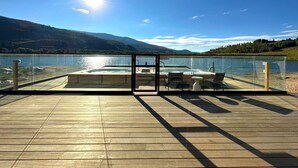 Eine Holzterrasse mit Whirlpool und Sitzbereich mit Blick auf einen See, im Hintergrund Berge.