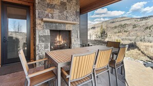 Eine Terrasse im Freien mit Kamin aus Stein, Holztisch und Stühlen.