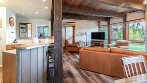 A spacious living area with a wooden ceiling, a large sofa, a TV, and a kitchen counter. - Walk to Gondola | Cozy 2BR Condo | Pool, Hot Tubs and Fireplace! (Steamboat Springs)