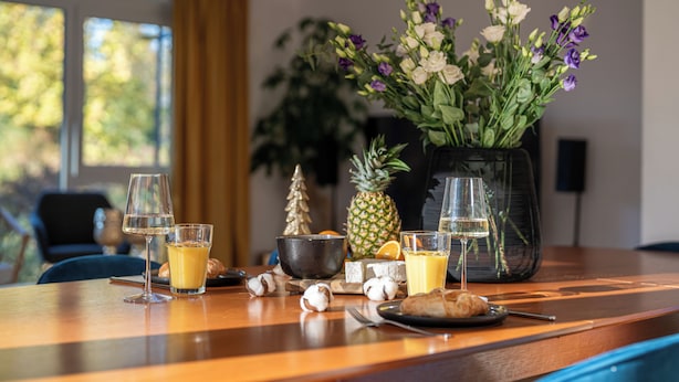 A breakfast table with a vase of flowers, a pineapple, a bowl, and two glasses of orange juice. - Liboria I Stylisches Haus 5min vom Starnberrger See (Starnberg)