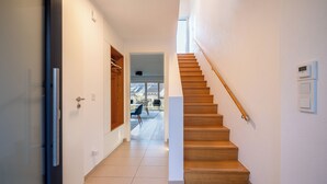 A modern interior with a wooden staircase, a hallway leading to a dining area, and a view through an open door. - Liboria I Stylisches Haus 5min vom Starnberrger See (Starnberg)