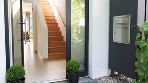 A modern entrance with a wooden staircase, a mail slot, and potted plants. - Liboria I Stylisches Haus 5min vom Starnberrger See (Starnberg)