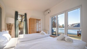 A hotel room with two beds, a wooden wardrobe, a large window with a view of the sea, and a lamp. - Liboria I Stylisches Haus 5min vom Starnberrger See (Starnberg)