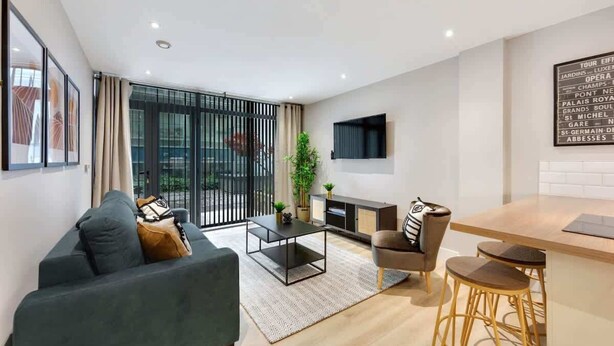 A modern living room with a sofa, coffee table, and bar stools. There is a TV mounted on the wall and a fireplace. - Host & Stay | Henry Street Chambers (Liverpool)