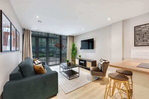 A modern living room with a sofa, coffee table, and bar stools. There is a TV mounted on the wall and a fireplace. - Host & Stay | Henry Street Chambers (Liverpool)