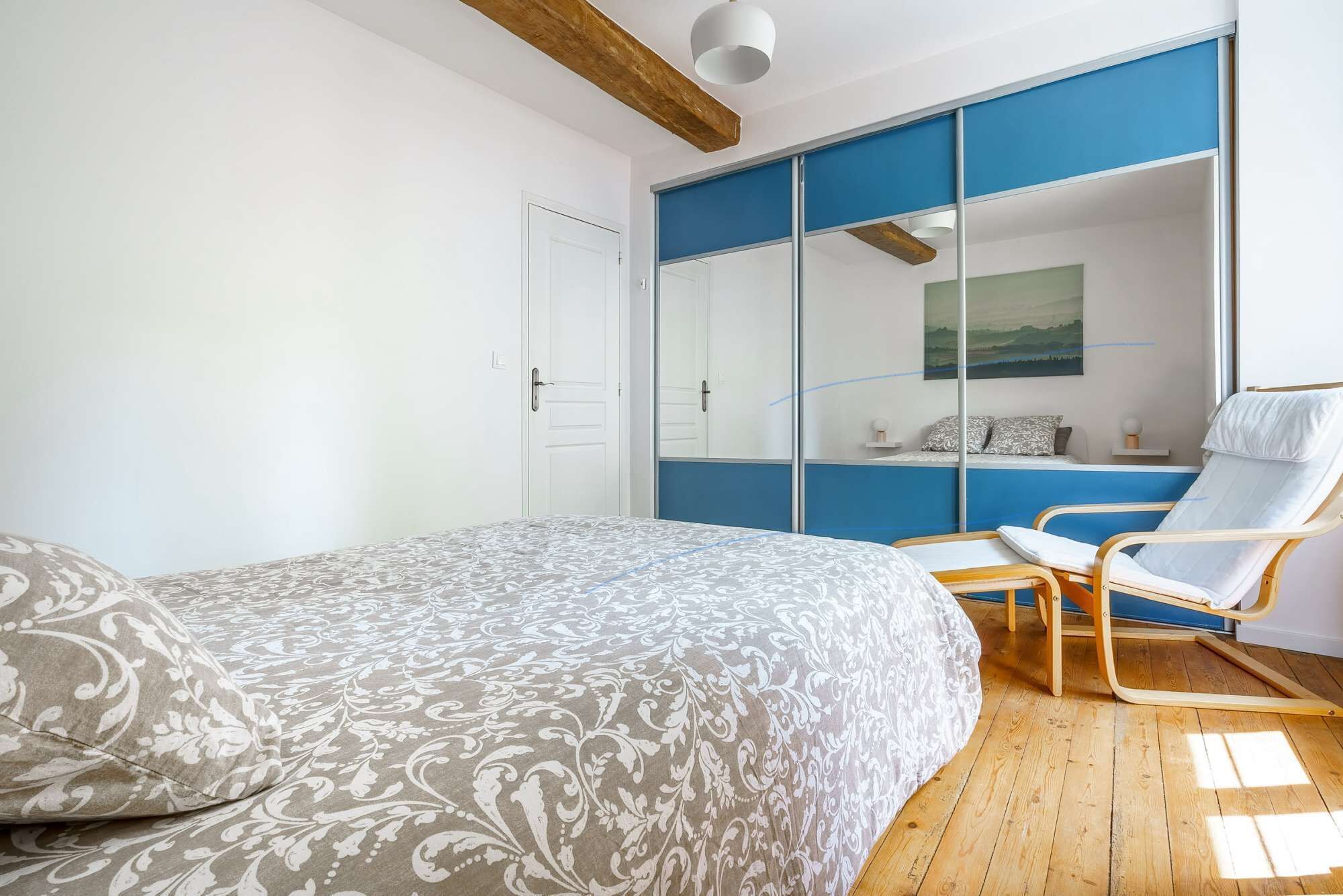 A bedroom with a bed, a chair, a wardrobe, and a painting on the wall.