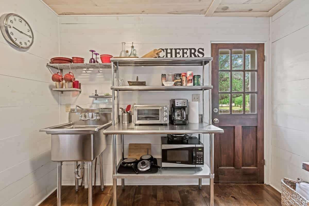 Una cocina compacta con electrodomésticos de acero inoxidable, un reloj y un letrero que dice 'CHEERS'.