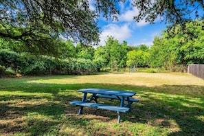 Ein Picknicktisch in einer grünen Wiese mit Bäumen und einem Zaun im Hintergrund.