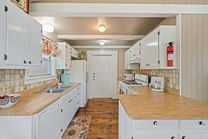A kitchen with white cabinets, a wooden countertop, a microwave, a coffee maker, and a fire extinguisher.