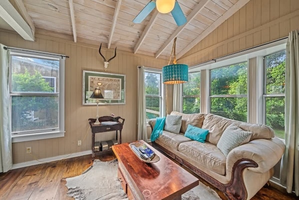 A cozy room with a wooden ceiling, a beige sofa with blue and gray cushions, a wooden coffee table, and a framed picture on the wall.