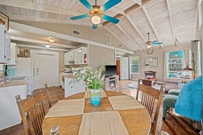 A spacious living room with a wooden dining table, chairs, and a ceiling fan.