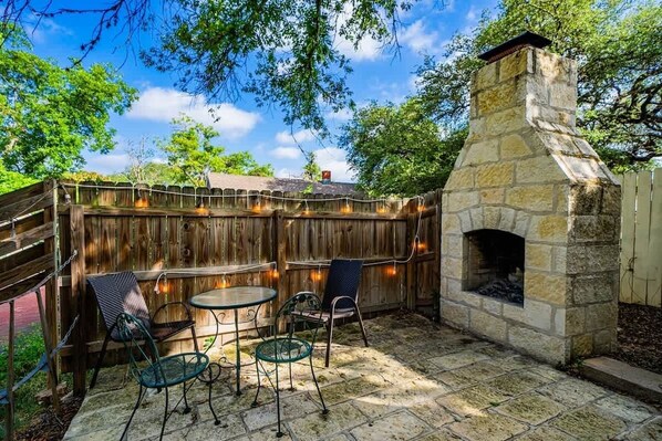 Un patio al aire libre con chimenea de piedra, cerca de madera y mobiliario exterior.