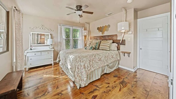 Une chambre à coucher comprenant un lit, une commode, un ventilateur de plafond, une fenêtre et une porte.