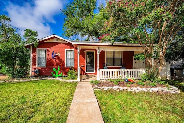 A red house with a porch, a mailbox, and a tree in the yard.