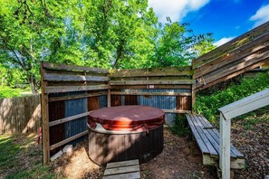A hot tub in a wooden outdoor enclosure with a wooden bench and a wooden deck.