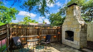 Une terrasse extérieure dotée d’une cheminée en pierre, d’une clôture en bois et de mobilier d’extérieur.