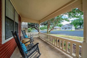 A covered porch with a white railing, two rocking chairs, and a wooden barrel.