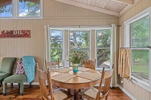 Un comedor con una mesa de madera, seis sillas y vista a árboles a través de ventanas amplias.