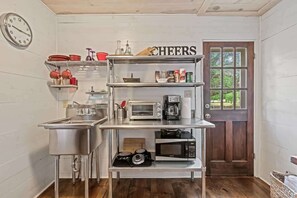 Cucina compatta con elettrodomestici in acciaio inossidabile, una sveglia e un cartello con la scritta 'CHEERS'.