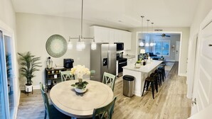 Cozinha moderna com ilha central, eletrodomésticos de aço inoxidável e área de refeições com mesa redonda e cadeiras.
