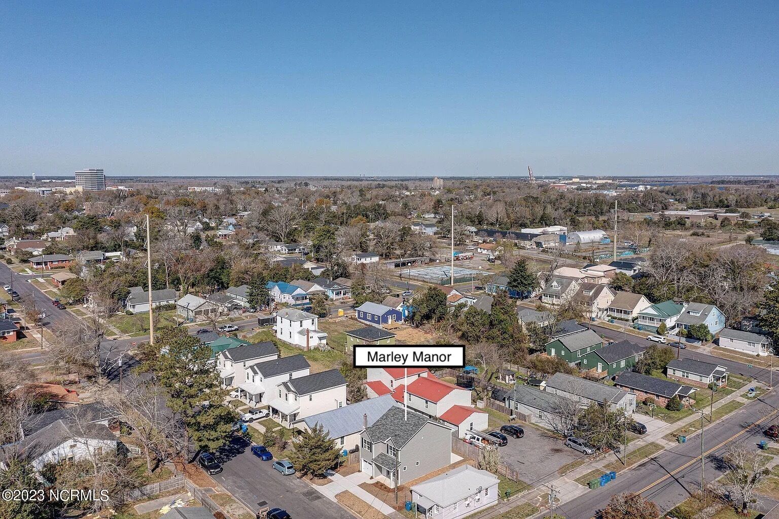 Un quartier résidentiel avec des maisons, un bâtiment imposant à toit rouge portant l’inscription « Marley Manor », et un ciel dégagé.