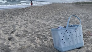 Uma praia com uma bolsa azul e chinelos na areia.