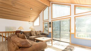 A spacious living room with a wooden ceiling, large windows, and a cozy seating area with a brown leather sofa and a coffee table.