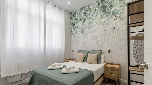 A bedroom with a bed, nightstands, a wooden dresser, and a wall with a leaf pattern. - Waou Fresh Confort I (Madrid)