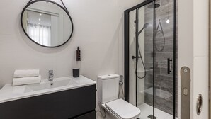 A modern bathroom with a glass-enclosed shower, a round mirror, a white sink, and a toilet. - Waou Fresh Confort I (Madrid)
