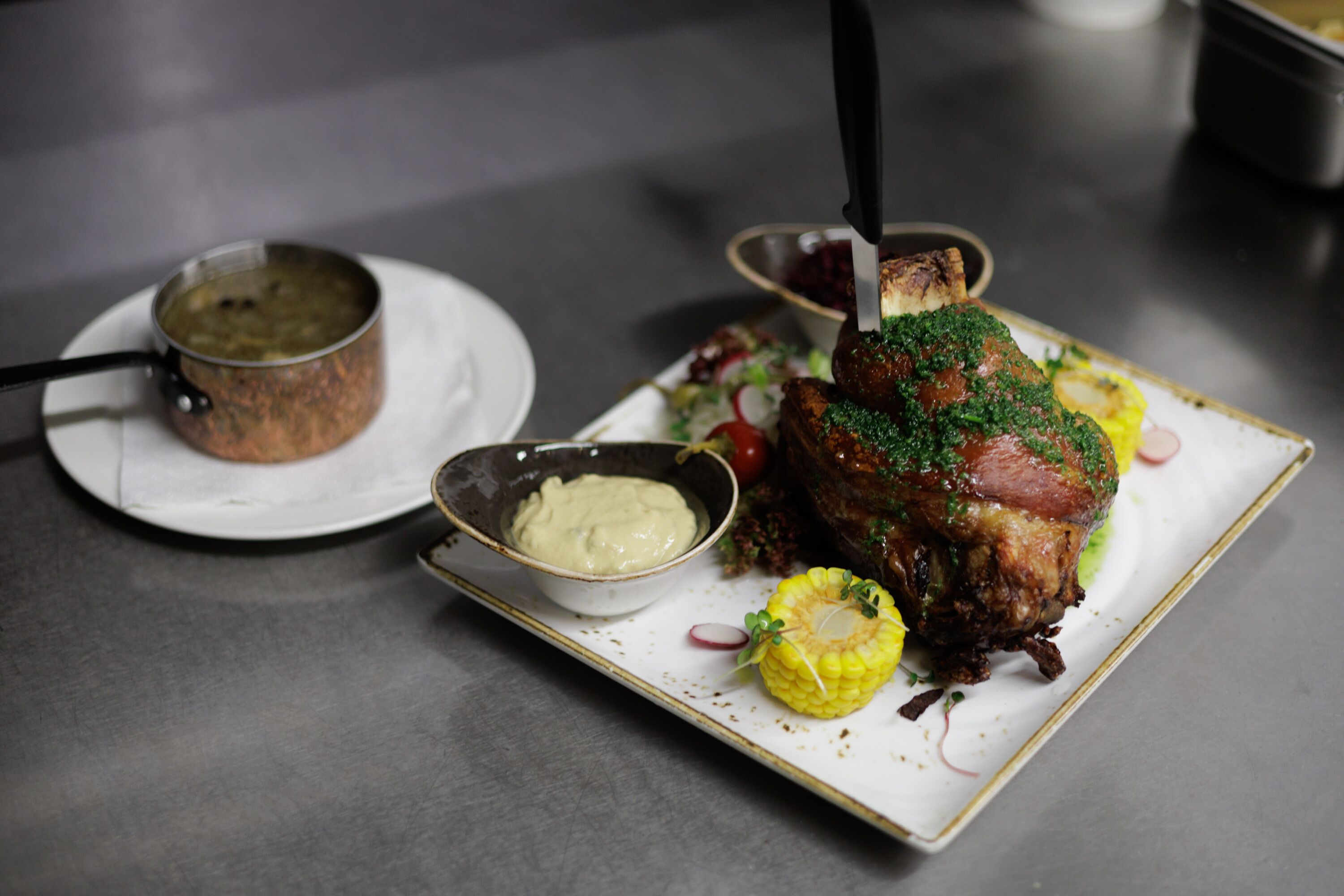 A plate with a roasted meat dish, a bowl of sauce, and a small pot on a table.