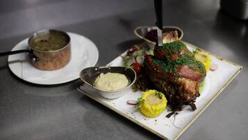 A plate with a roasted meat dish, a bowl of sauce, and a small pot on a table.