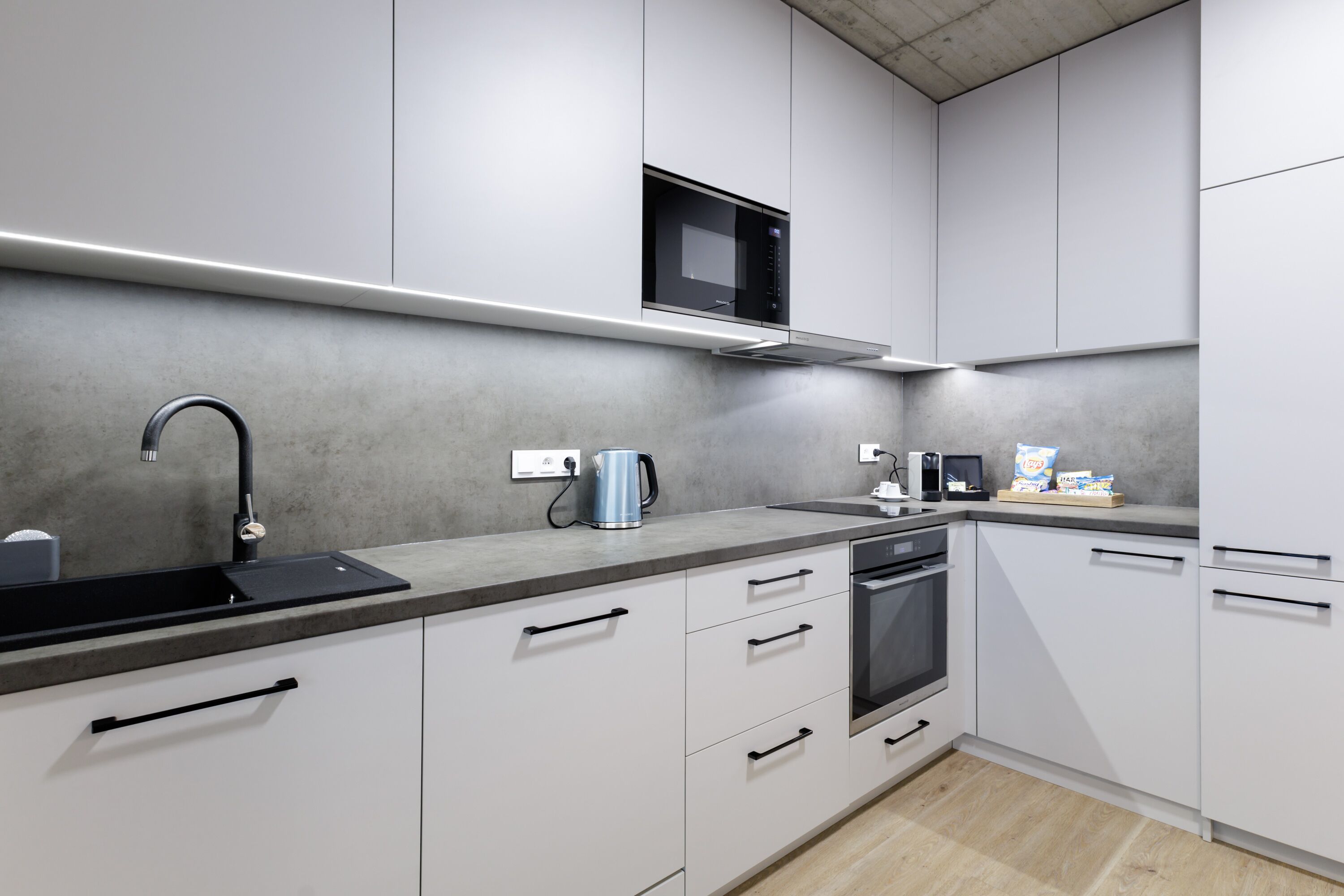 A modern kitchen with white cabinets, a stainless steel sink, a microwave, and a coffee maker.