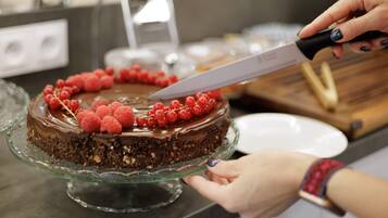 A person cutting a chocolate cake with raspberries on a glass cake stand.