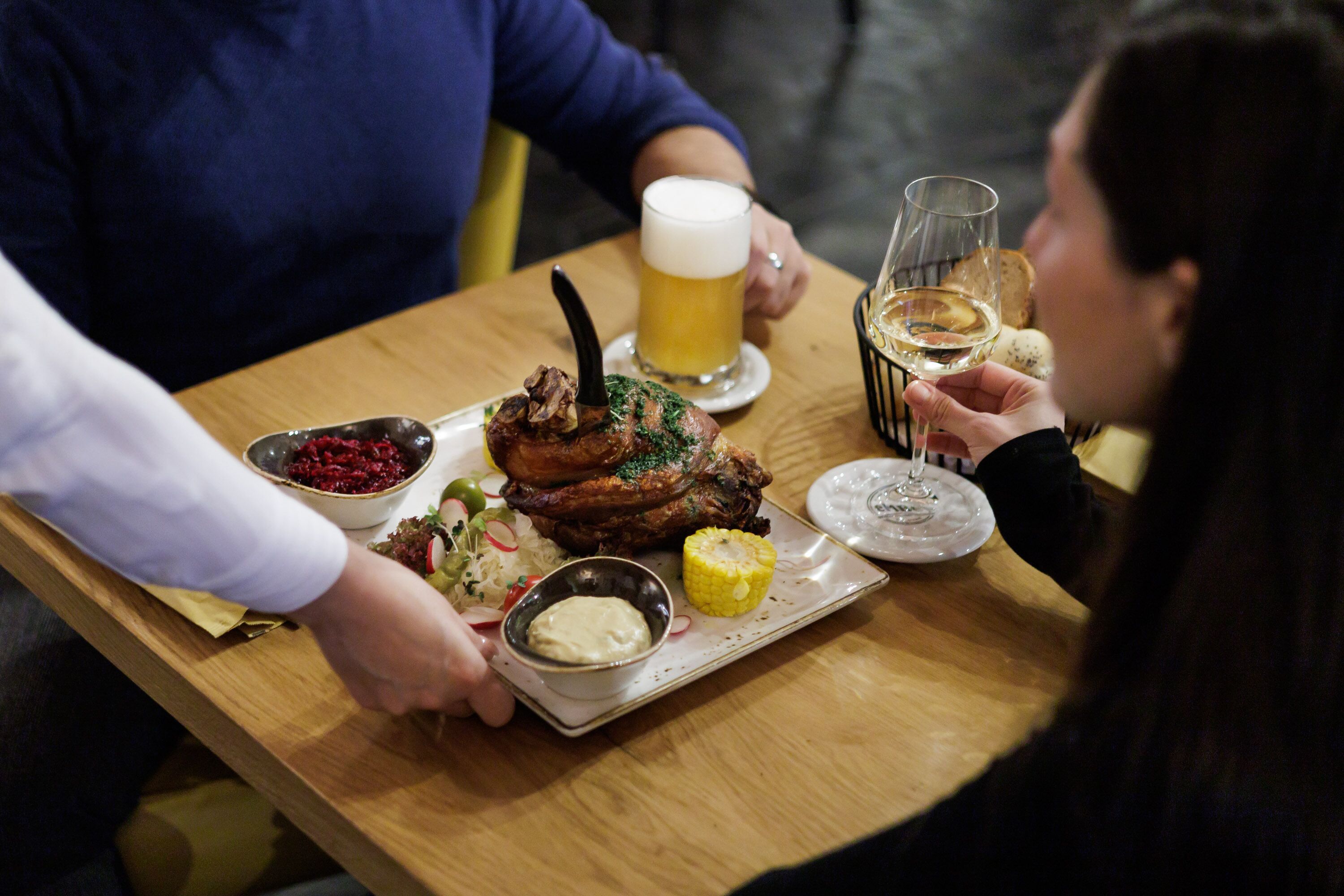 A dining table with a plate of food, a glass of beer, and a glass of wine.