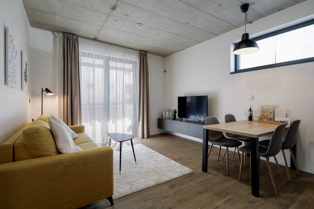 Un salon moderne comprenant un canapé, une table à manger avec des chaises, un téléviseur et une grande fenêtre avec des rideaux.