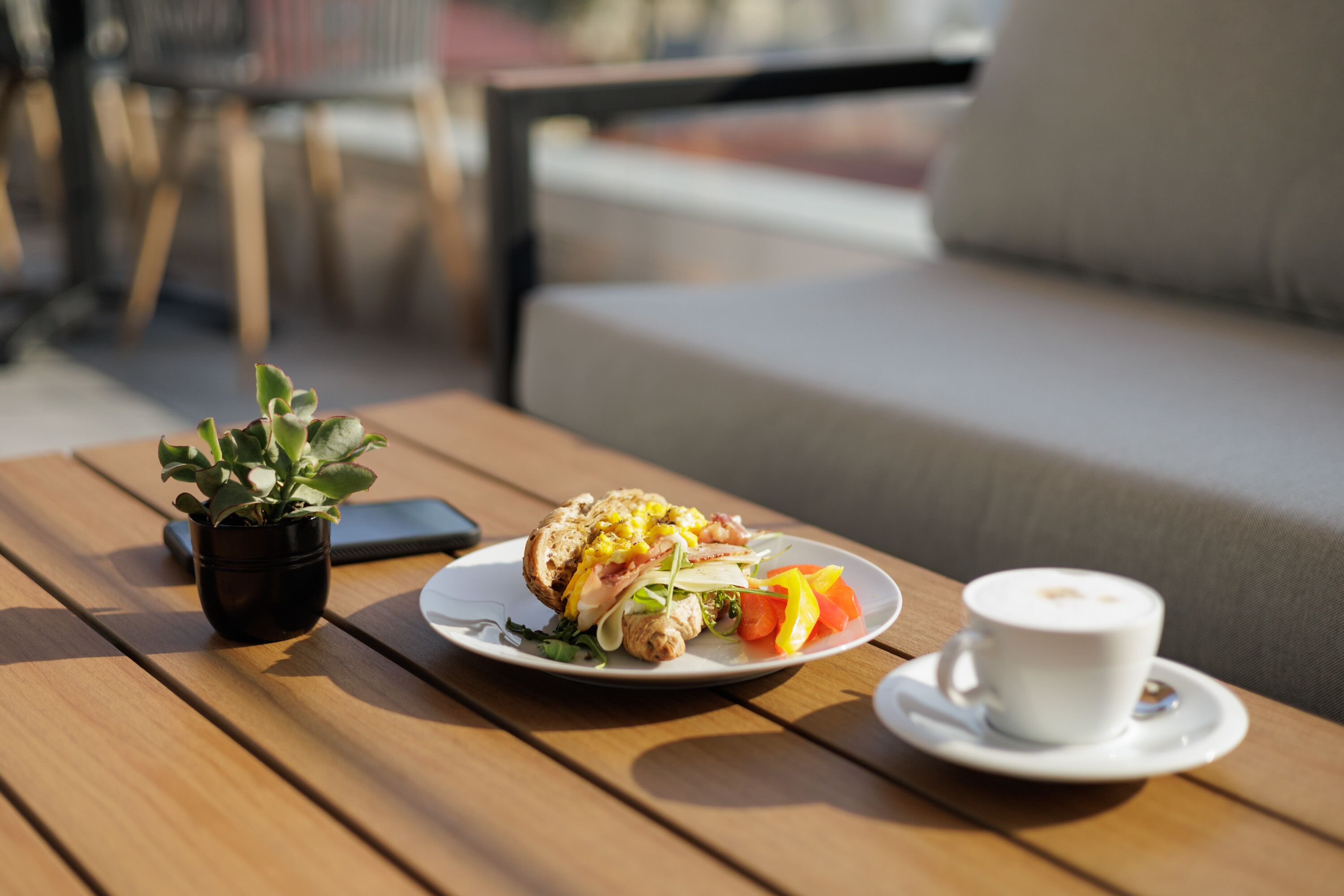 A wooden table with a sandwich, a cup of coffee, and a small potted plant.
