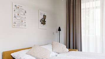 Une chambre d’hôtel avec un lit, deux oreillers, une table de chevet, une lampe et une fenêtre avec des rideaux.