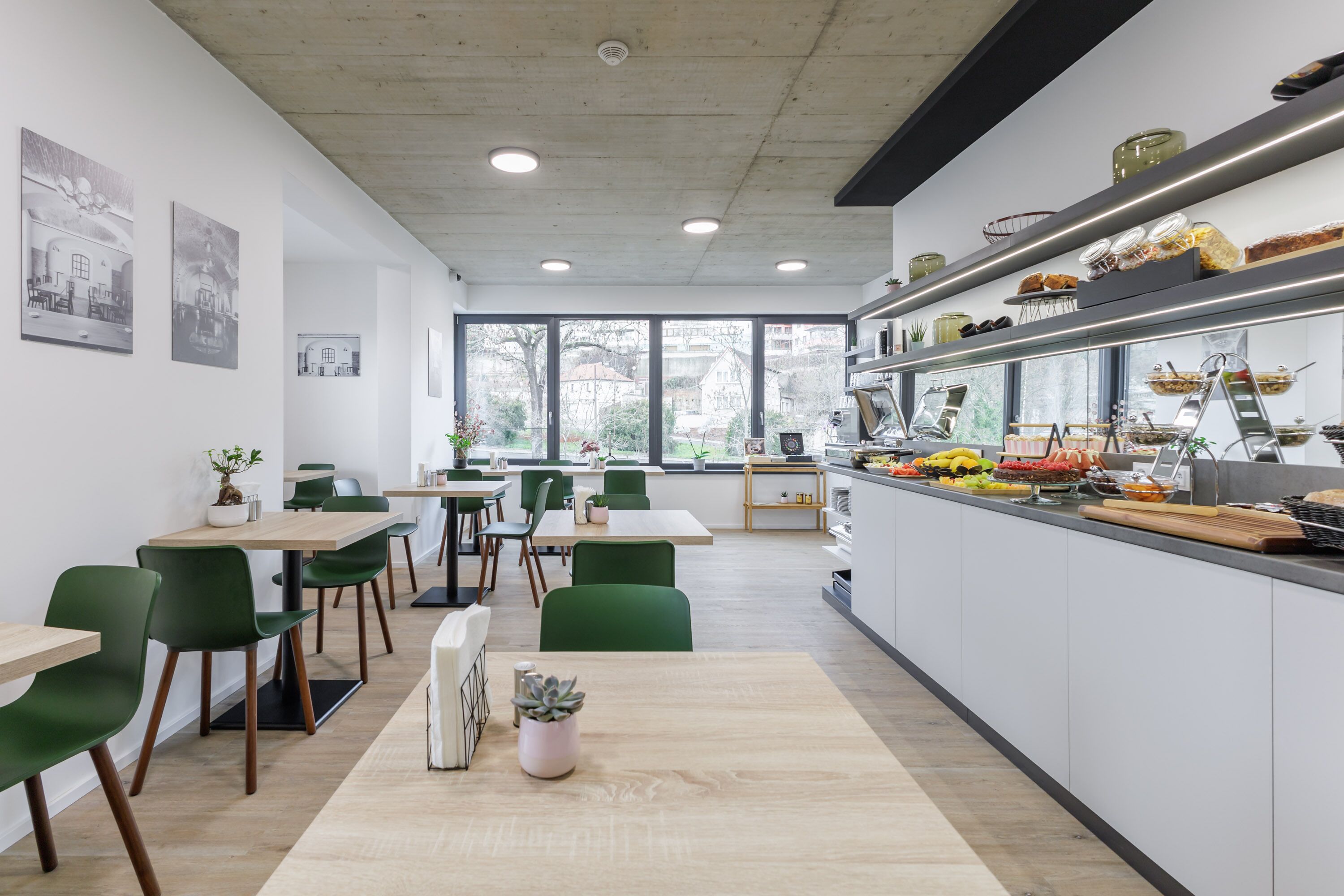 Un restaurante moderno con sillas verdes, mesas de madera y una barra de cocina con diferentes alimentos.