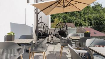 Un patio al aire libre con una mesa y sillas, un sillón colgante y un paraguas grande.