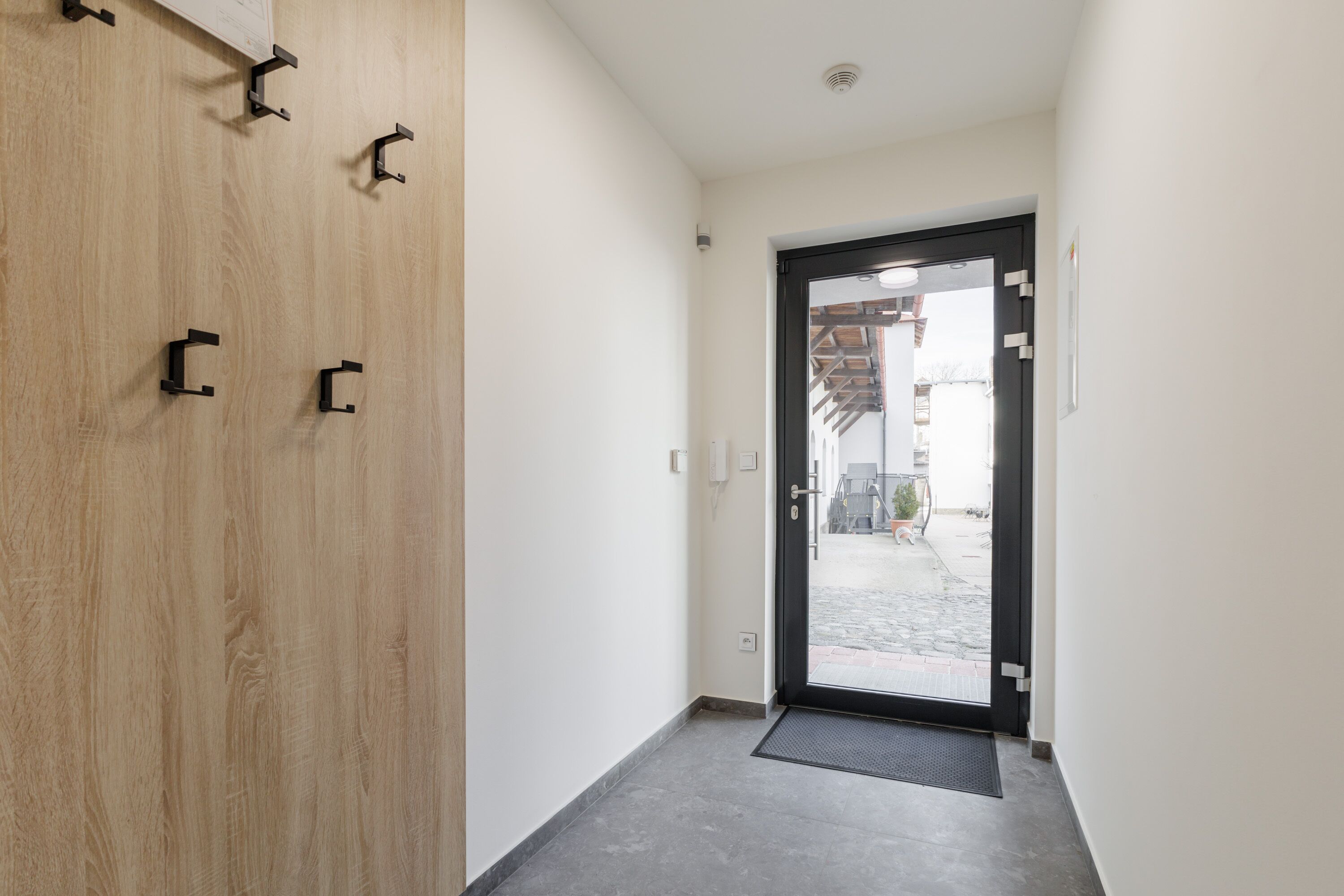 Un pasillo con una puerta de madera y una puerta negra que da al exterior.