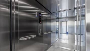 Un ascensor modern amb pantalla digital, parets metàl·liques i una porta de vidre transparent.