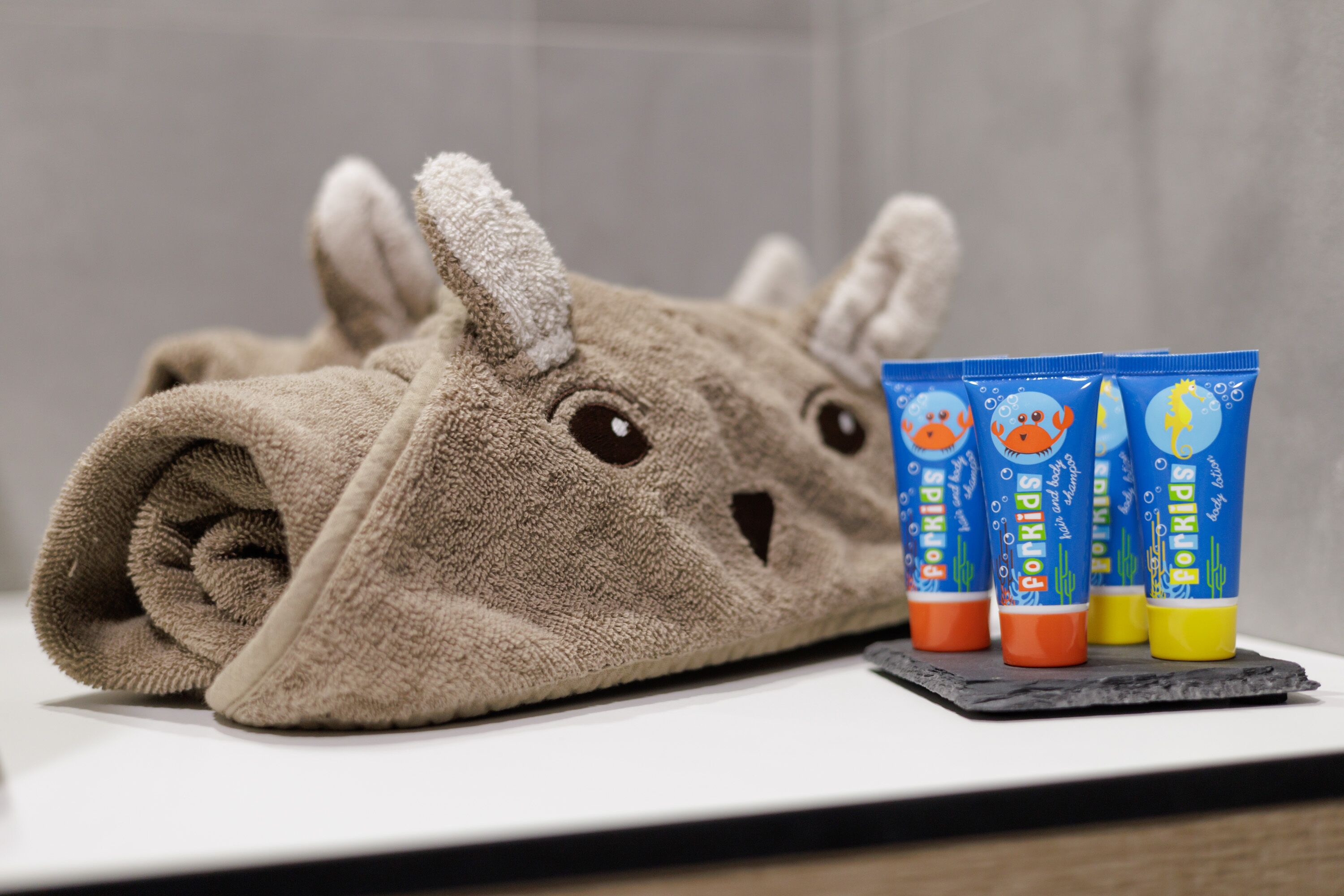 A towel with a cartoon character design, a set of blue tubes with colorful caps, and a dark slate coaster.