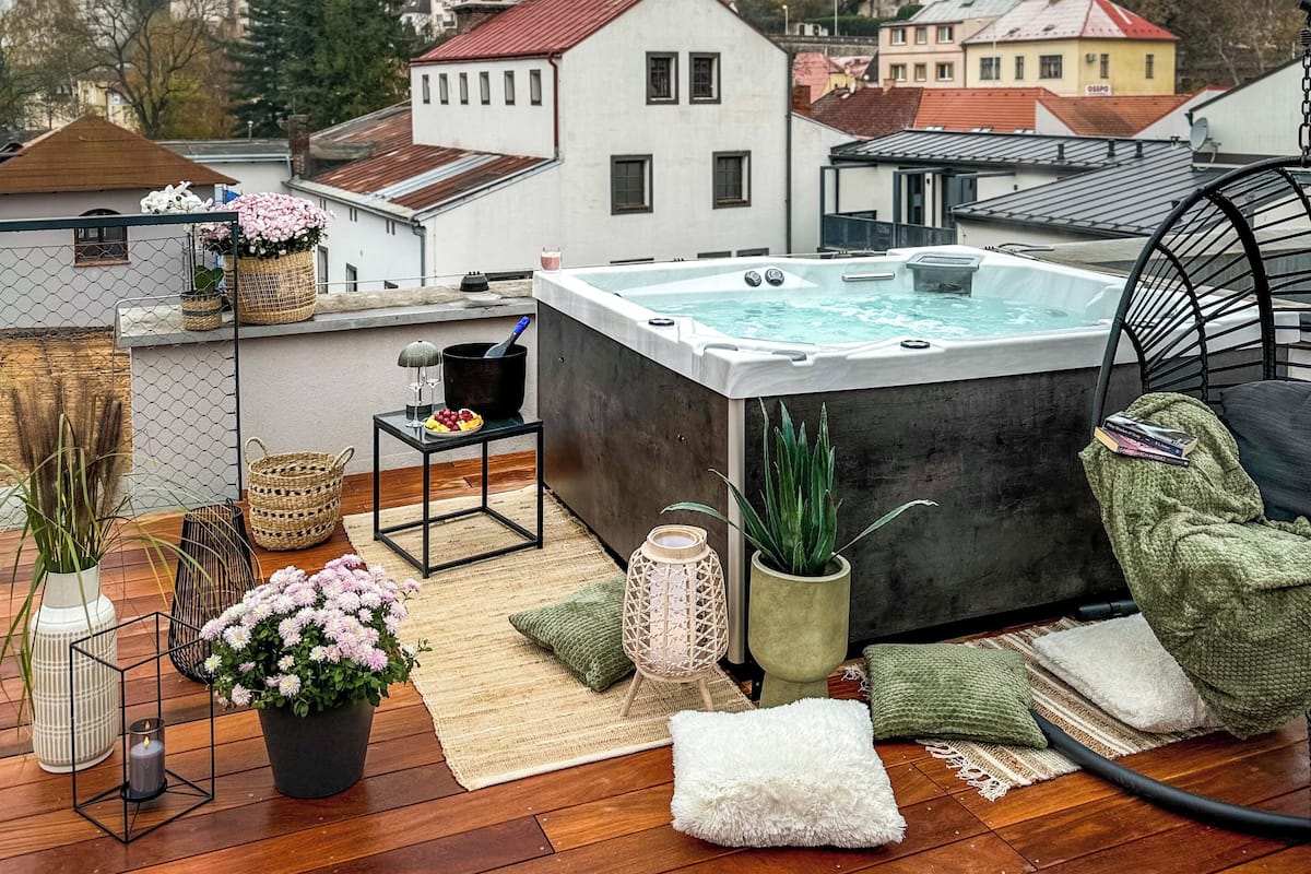 Une terrasse sur le toit dotée d’un jacuzzi, d’un plancher en bois et offrant une vue sur le paysage urbain, notamment une haute cheminée.
