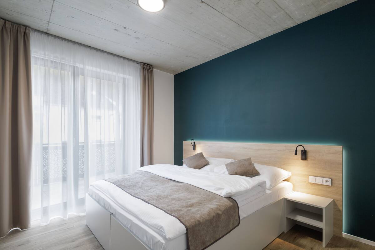 Une chambre moderne avec un grand lit, des tables de chevet et une vue dégagée à travers des rideaux légers.