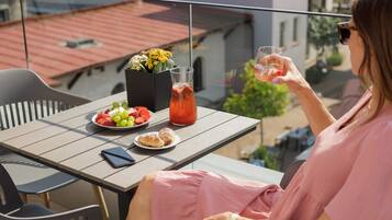 A balcony with a table set for a meal, including fruits, a drink, and pastries.