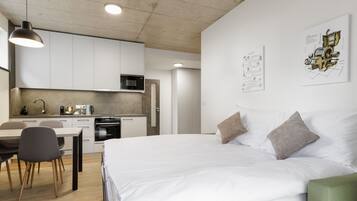 A modern hotel room with a large bed, a desk, and a kitchenette.