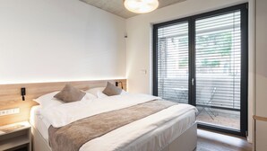 Een moderne slaapkamer met een groot bed, een houten hoofdbord, een nachtkastje en uitzicht door een schuifdeur op een buitenruimte.