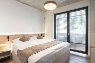 Un dormitorio moderno con una cama grande, cabecera de madera, mesita de noche y vistas a un área exterior a través de una puerta corrediza de vidrio.