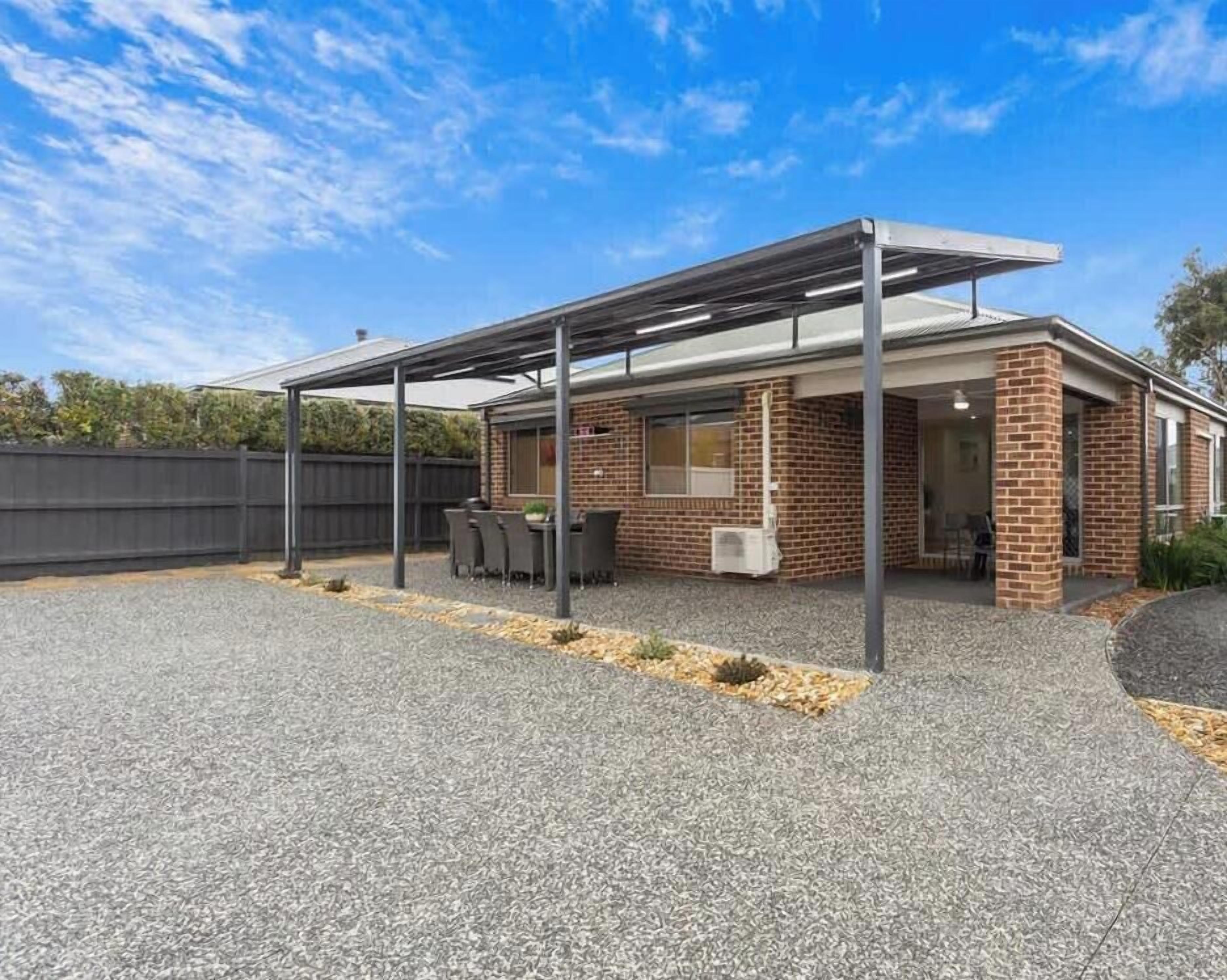 A single-story building with a covered patio area, a brick exterior, and a gravel driveway.
